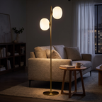 Brass and white glass two-light floor lamp beside a sofa in the evening
