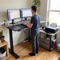 L shaped electric standing desk with file cabinet surface in a home office corner
